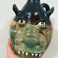 a person is holding a ceramic jug with a dragon face on it