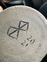 a person is holding a piece of clay with a symbol on it