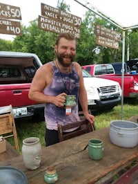 a man with a beard standing next to a table full of pots