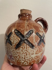 a person holding a brown vase with a cross on it